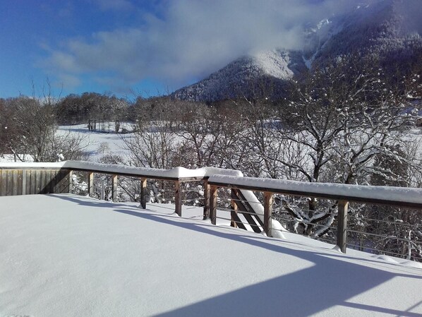 A snowy landscape with a wooden railing and a view of snow-covered trees and mountains.