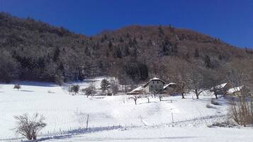 Paisaje nevado con una casa en una colina, rodeada de árboles y un cielo azul despejado.