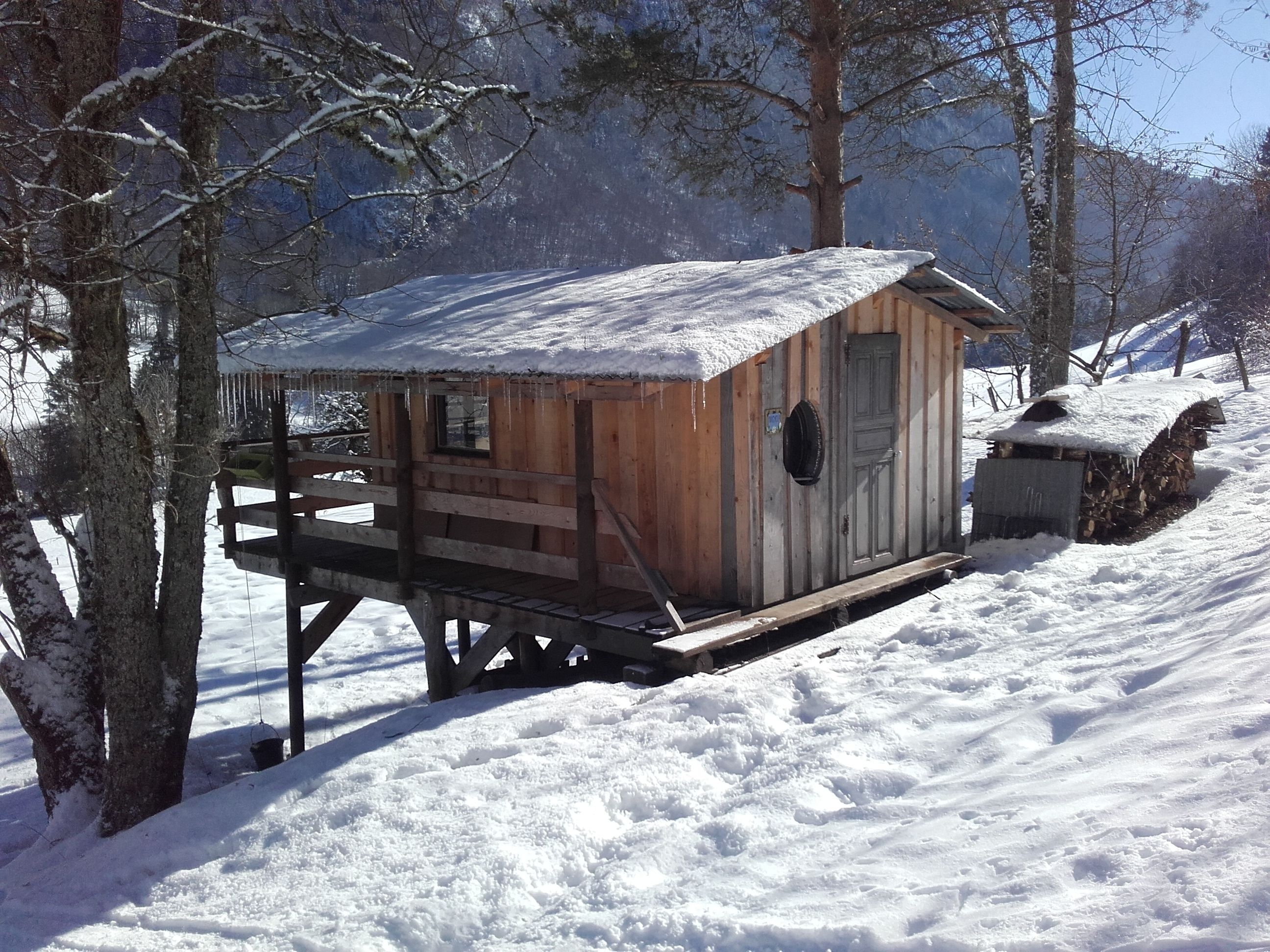 A wooden cabin with a snow-covered roof, situated in a snowy forest.