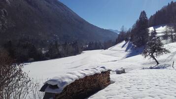 Een besneeerd landschap met een houten gebouw, waarschijnlijk een chalet, omringd door bomen en bergen.