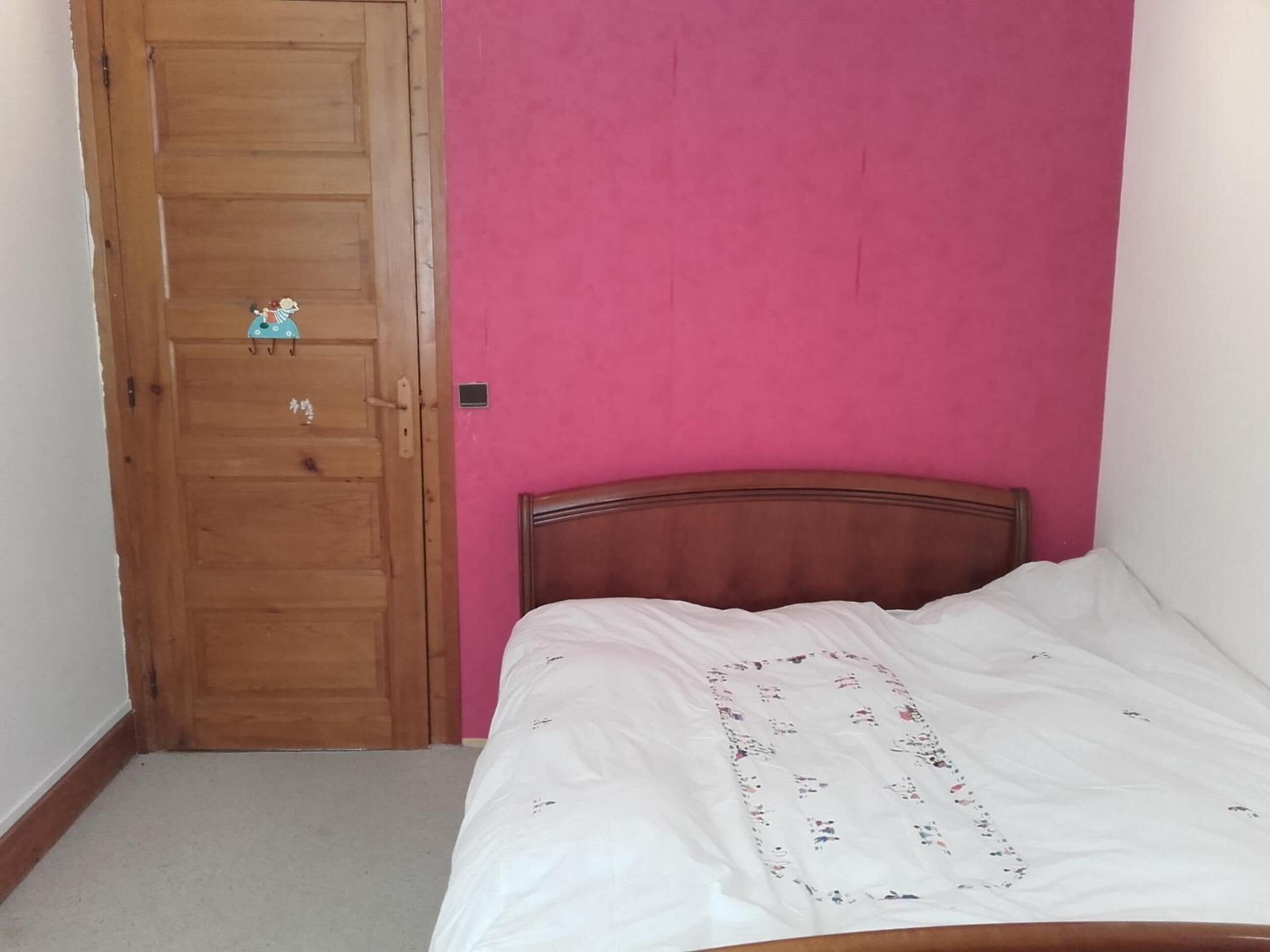 Ein Schlafzimmer mit Holztür, rosa Wand und Bett mit weißer Bettdecke.