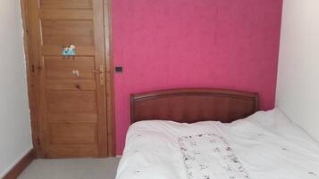 Ein Schlafzimmer mit Holztür, rosa Wand und Bett mit weißer Bettdecke.