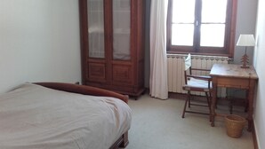 Une chambre avec une armoire en bois, un lit, un bureau avec une lampe et un radiateur.