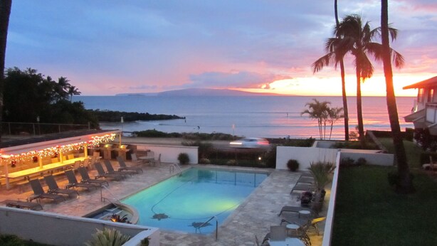 Ein Swimmingpool mit Liegestühlen und Blick auf den Ozean bei Sonnenuntergang.