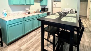 Een moderne keuken met blauwgroene kastjes, een zwarte eettafel en een houten vloer.