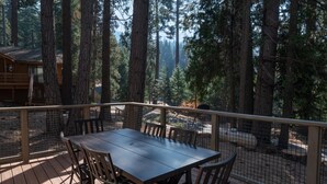 Eine Holzdar Terrasse mit Tisch und Stühlen, umgeben von einem Metallgeländer, mit Blick auf einen bewaldeten Bereich.