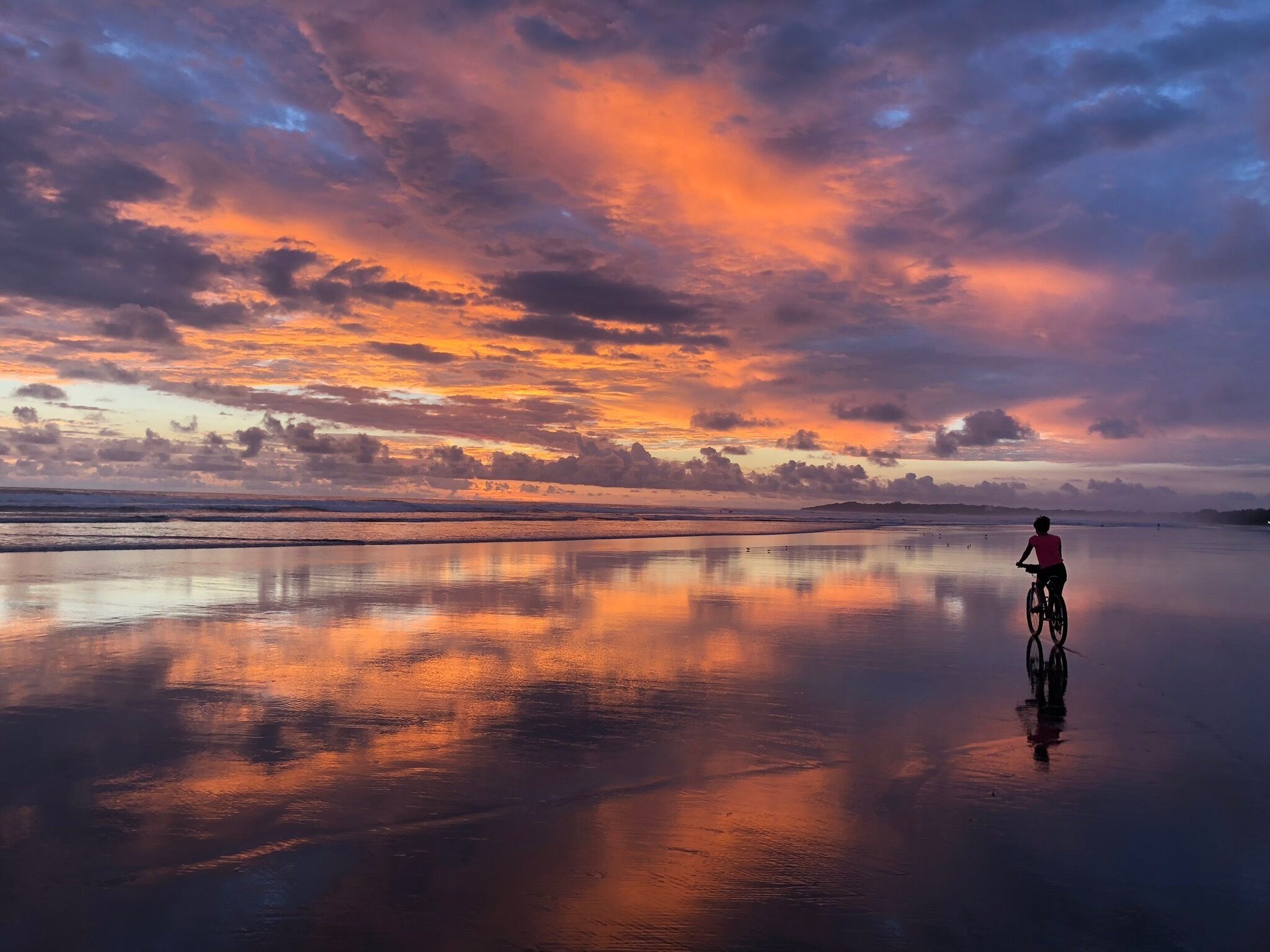 A person riding a bicycle on a reflective water surface with a sunset in the background.