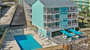 Un hotel de varios pisos con zona de piscina, balcones y vistas a la playa.