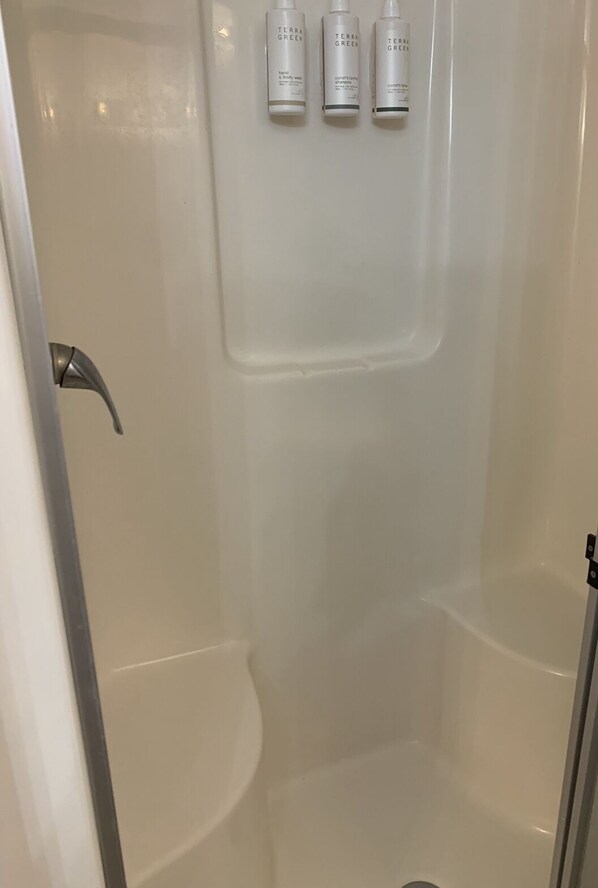 A shower area with a white interior, a showerhead, and three bottles of Terra Green hand and body wash on the wall.