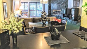 Un salon avec un canapé, une table basse et une cheminée. Il y a une grande fenêtre et un lustre.