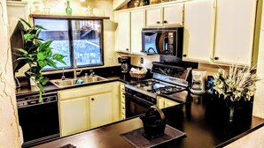 Une cuisine équipée d’une cuisinière, d’un évier et de placards. Il y a une fenêtre au-dessus de l’évier et une plante sur le plan de travail.