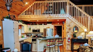 A cozy cabin interior with a kitchen, dining area, and a staircase leading to an upper level.