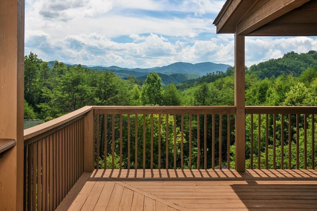 Eine Holzdielen-Terrasse mit Geländer mit Blick auf einen bewaldeten Gebirgszug.