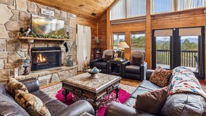 A cozy living room with a stone fireplace, leather furniture, and a large window overlooking a scenic landscape.