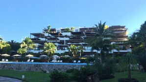 Un hôtel à plusieurs étages doté de balcons, de palmiers et d’un espace piscine.