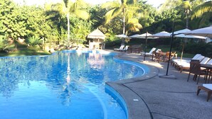 Une piscine entourée d’une végétation luxuriante, avec des chaises longues et des parasols.