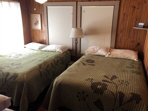 A room with two beds, each with a floral-patterned bedspread, a bedside lamp, and a framed picture on the wall.