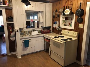A compact kitchen with white cabinets, a stove, and a sink. - Bandera River House | Bandera | Deer | Private (Bandera)