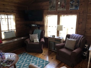 A cozy cabin interior with two armchairs, a television, and a window with curtains.
