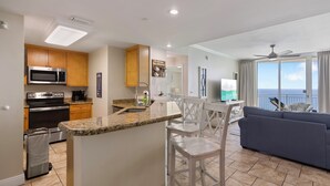 A modern kitchen with a microwave, stove, and coffee maker, a dining area with a white table and chairs, and a balcony with a view. - Aqua 2102 Luxury Gulf Front Escape, Beach Chairs, Walk to Pier Park (Panama City Beach)