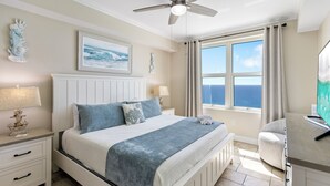 A bedroom with a bed, nightstands, a ceiling fan, a window with curtains, and a view of the ocean. - Aqua 2102 Luxury Gulf Front Escape, Beach Chairs, Walk to Pier Park (Panama City Beach)
