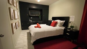 A bedroom with a bed, a desk, and a chair. There are framed pictures on the wall. - The Cozy Red Cabin  (Bellevue)