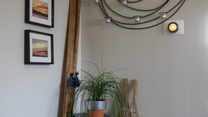 A room with a wooden floor, a black vase with a plant, a black sign with text, a wooden chair, and a wall-mounted light fixture. - The Cozy Red Cabin  (Bellevue)