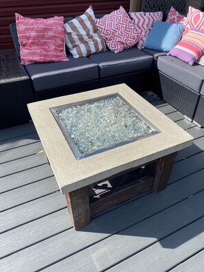 Een vierkante tafel met een glazen blad, omgeven door een houten frame, op een terras met grijze houten planken.