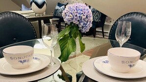 Una mesa de vidrio redonda con dos cuencos blancos y dos copas de vino, sobre un tapete estampado.