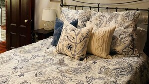 Un dormitorio con cama, mesita de noche, lámpara, un cuadro y una puerta.
