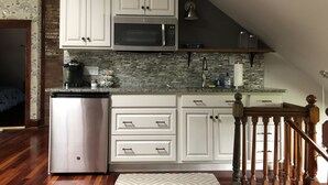 Una cocina compacta con armarios blancos, un microondas integrado y un refrigerador de acero inoxidable.