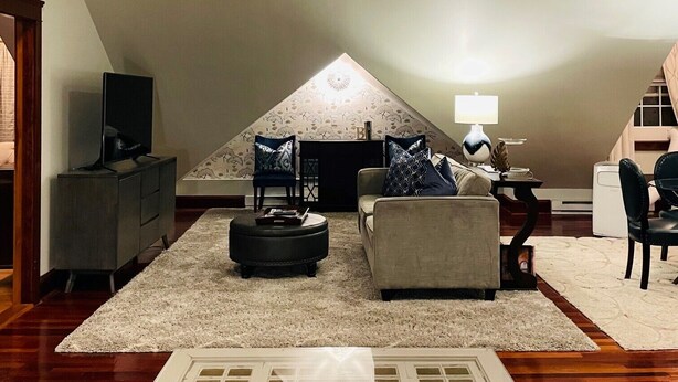 Un salón tipo loft con techo alto, chimenea, sofá, televisor y ventana.