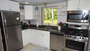 A modern kitchen with stainless steel appliances, white cabinetry, a window with a view of trees, and a dish rack with utensils. - Lakefront Cottage in Manitou Beach - Three Bedroom Cottage, Sleeps 8 (Manitou Beach)