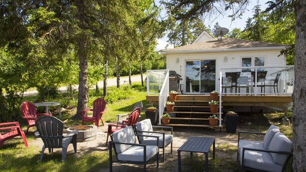 A cozy outdoor patio area with seating and a deck overlooking a house. - Lakefront Cottage in Manitou Beach - Three Bedroom Cottage, Sleeps 8 (Manitou Beach)