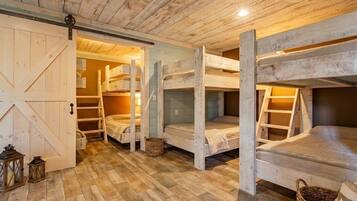 A rustic cabin interior with wooden bunk beds, a sliding barn door, and a herringbone-patterned floor.