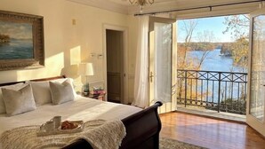 A bedroom with a large bed, a chandelier, a painting, a nightstand, and a view of a river through a balcony. - Large House with Lake Views, pool table and Private Boat Dock (Gainesville)