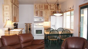 A compact kitchen with wooden cabinets, a dining table with chairs, and a brown leather sofa.