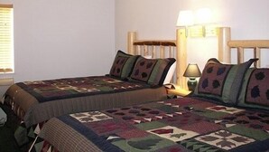A bedroom with two beds, each with a quilted bedspread and matching pillows. There is a nightstand with a lamp between the beds.
