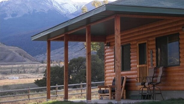 A log cabin with a porch, wooden chairs, and a view of mountains.