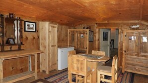 A rustic wooden interior with a dining table, chairs, a refrigerator, and a patterned rug. - Corazones Draw Ranch: Spacious Home on 400 acres (Brewster County)