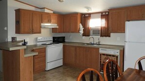 A compact kitchen with wooden cabinets, a stove, microwave, and a dishwasher. - Corazones Draw Ranch: Spacious Home on 400 acres (Brewster County)