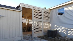 A covered outdoor area with a stone patio, a white fence, and a window on the adjacent building. - Corazones Draw Ranch: Spacious Home on 400 acres (Brewster County)