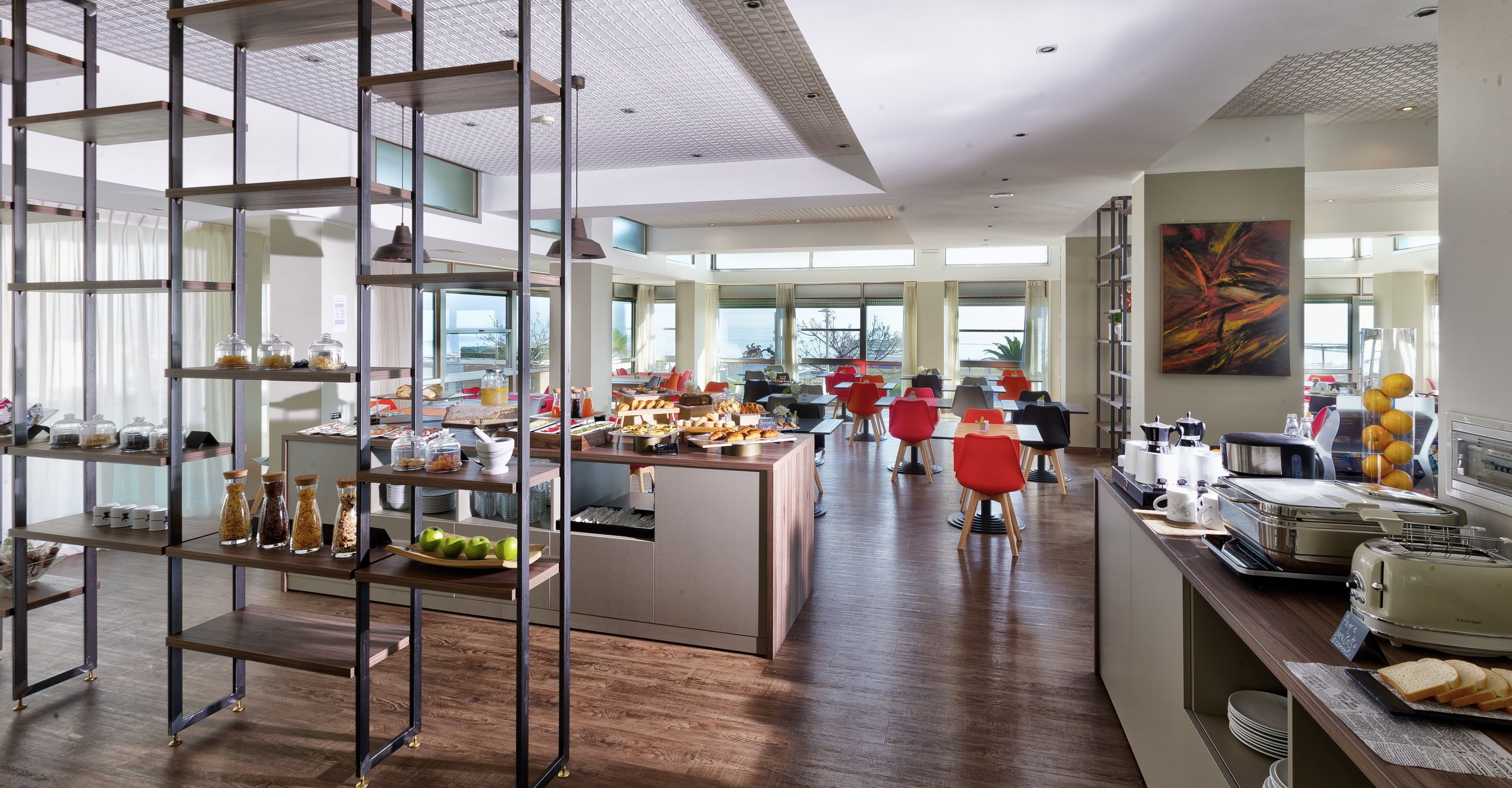 A modern hotel dining area with a buffet setup, a central island with seating, and a view of the outdoors.