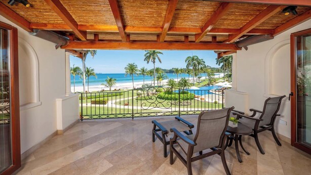 A balcony with a view of a beach and pool, featuring a wooden ceiling and two chairs. - Upscale Two-Bedroom Condo in Playa Flamingo with Beautiful Oceanfront Views (Playa Flamingo)