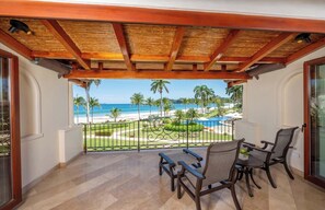 Een balkon met uitzicht op een strand en zwembad, met een houten plafond en twee stoelen.