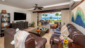 A living room with a large flat-screen TV, leather sofas, a coffee table, and a view of the beach. - Upscale Two-Bedroom Condo in Playa Flamingo with Beautiful Oceanfront Views (Playa Flamingo)