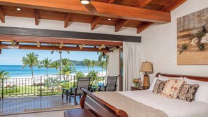 A hotel room with a balcony overlooking a beach, a bed with patterned pillows, and a painting on the wall. - Upscale Two-Bedroom Condo in Playa Flamingo with Beautiful Oceanfront Views (Playa Flamingo)