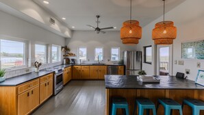 Une cuisine moderne avec des meubles en bois, un îlot central doté de tabourets et de grandes fenêtres.
