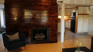 Un salon moderne avec un mur en bois, une cheminée, un fauteuil noir et une table à manger agrémentée d’un vase.