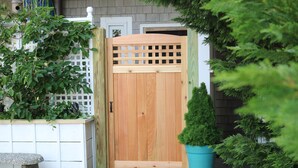 Une porte en bois ornée d’un motif en treillis, un arbuste à feuilles persistantes en pot et un banc en pierre.
